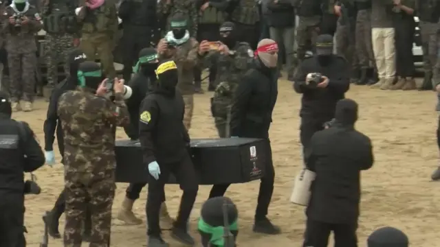 Four men wearing face coverings and headbands carry a coffin through the square, surrounded by crowds