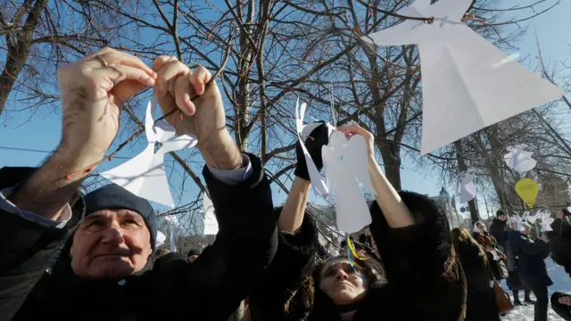 An man and a woman hang up symbolic paper-made angel figures on tree branches in Kyiv.