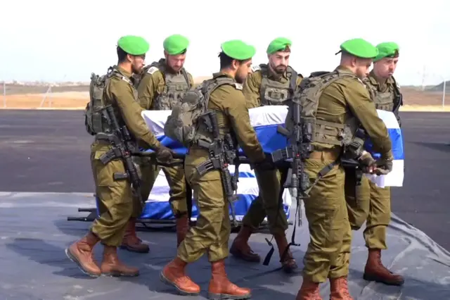 IDF soldiers in green berets carry one of the coffins which is draped in an Israel flag