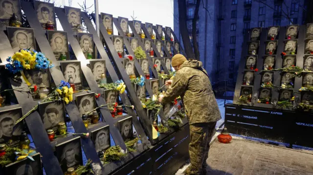 A soldier at the memorial for fallen Ukrainians, whose pictures are surrounded by flowers