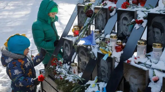 Two children, one wearing blue and another in green, place flowers on memorial showing photos of those who died in the protests.