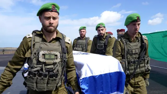 Sullen-looking IDF soldiers in green berets carry one of the coffins which is draped in an Israel flag