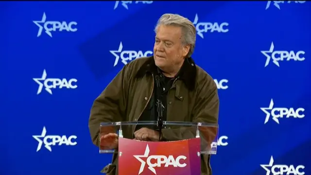 Bannon in brown jacket in front of blue background with CPAC logo