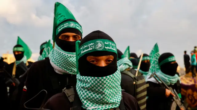 Hamas members in black balaclavas with green headbands and white and green keffiyehs carry guns as they stand guard in Khan Younis