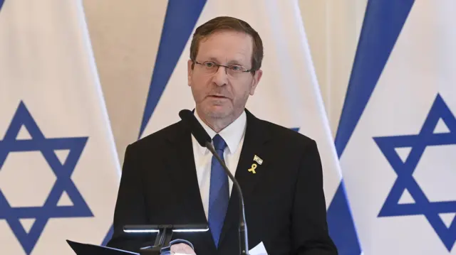 Isaac Herzog speaks into a microphone, flanked by Israeli flags