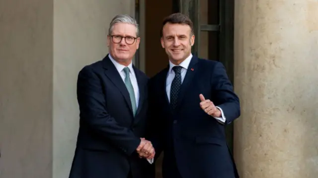 France s President Emmanuel Macron welcomes Britain s Prime Minister Keir Starmer. They shake hands and are both wearing suits.