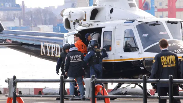 Luigi Mangione in orange jumpsuit stepping out of NYPD helicopter with police officers standing either side of the exit