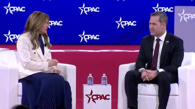 Waltz sitting in white chair on the stage next to a female presenter