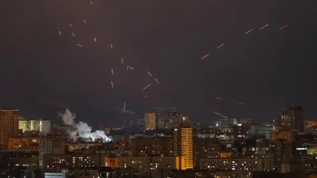 A number of orange and red streaks are seen crossing through the night sky above Kyiv's city skyline.