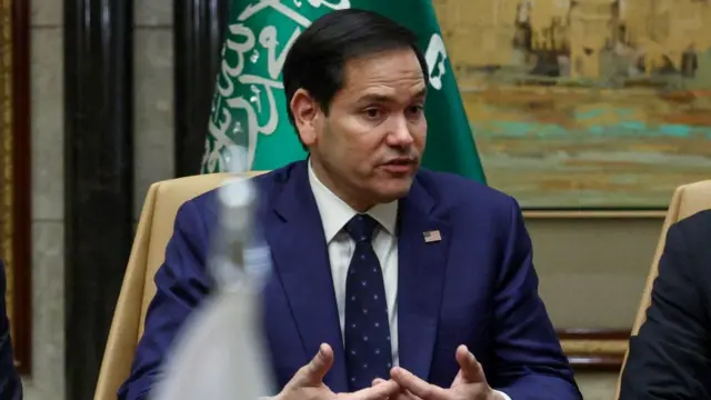 Marco Rubio speaks sat at a table in front of a flag