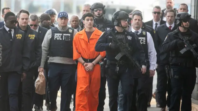 Mangione, wearing an orange jumpsuit, flanked by scores of police officers - some carrying guns