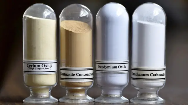 Four glass vials of rare earth minerals standing on a wooden desk