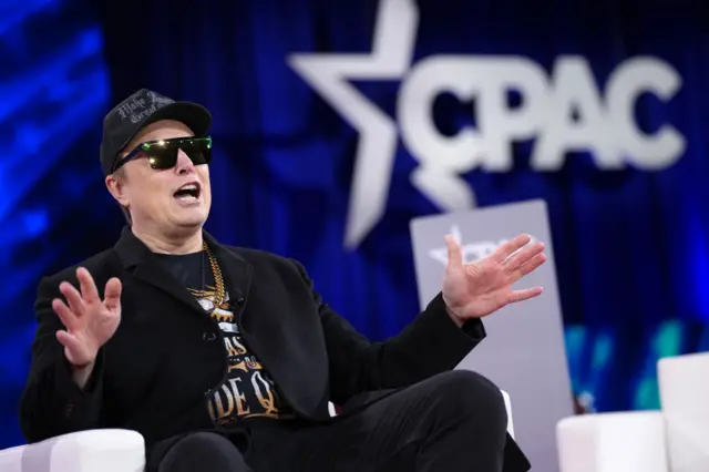 Man sits in sun glasses with CPAC banner in background