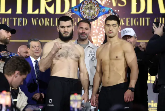 Artur Beterbiev and Dmitry Bivol standing side by side with Eddie Hearn behind them