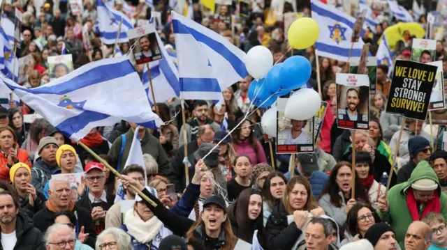 Crowds gather holding Israel flags and banners with pictures of hostages on.