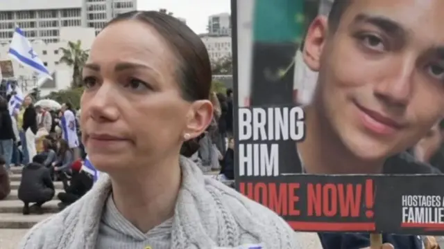 Yael Alexander, mother of American-Israeli hostage, Edna Alexander, pictured behind her on missing billboard