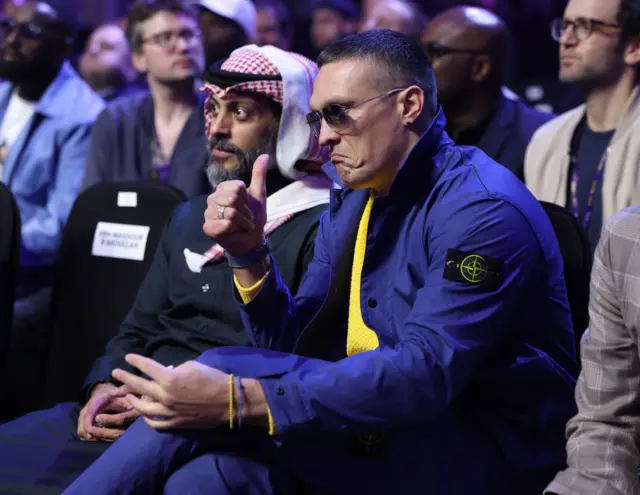 Oleksandr Usyk wearing a blue jacket puts his thumb up