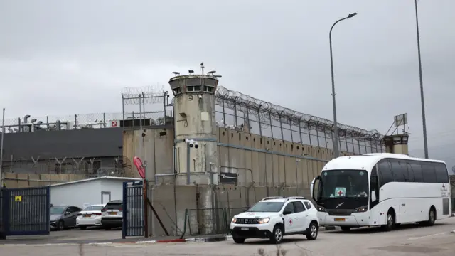 International Committee of the Red Cross vehicles outside Ofer Prison. It is a white coach and white car with Red Cross icon to the side and front parked to the left of the building, other cars parked inside the courtyard to the left of the frame