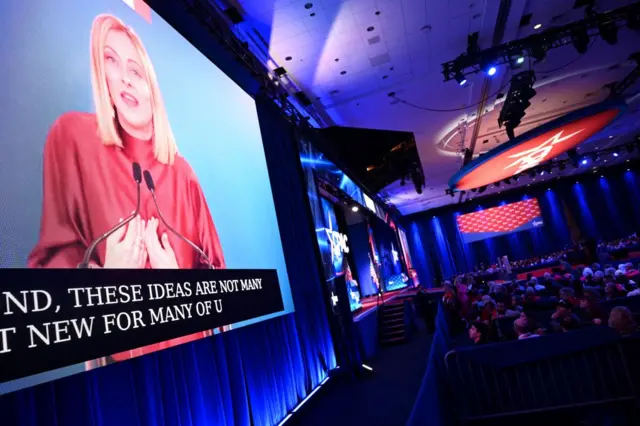 Woman shown on TV screen as audience watches