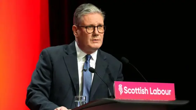 Starmer stood at a lectern with the words Scottish Labour in white on a red sign at the front. He speaks into two microphones.