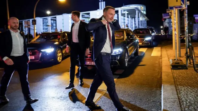 Christian Lindner walking across a road, fixing the collar of his jacket.