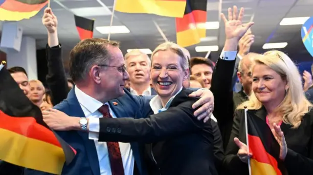 arty co-leaders Tino Chrupalla and Alice Weidel in an embraced, as people wave German flags around them