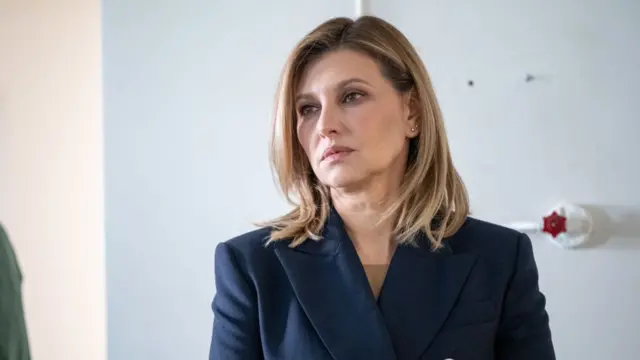 Headshot of Zelenska, who has short blonde hair and wears a navy blazer with gold buttons. She looks serious