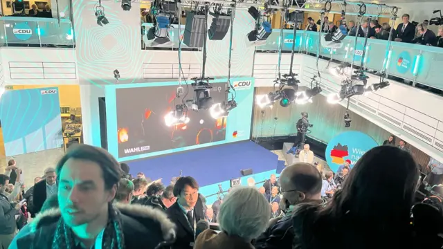 The stage ready for speeches at the CDU headquarters, and lots of media standing around, with a lot of stage lights hanging from the ceiling.