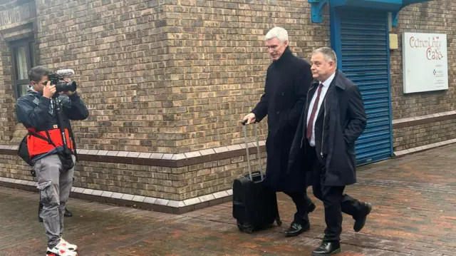 Mike Amesbury walks alongside another man towards a court building as photographer takes pictures