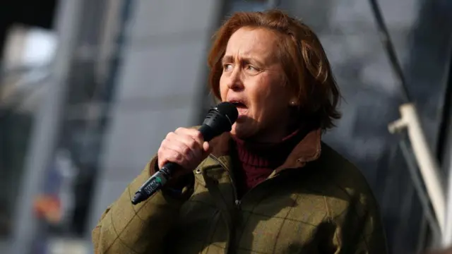 Beatrix von Storch speaking into a microphone, dressed in a green coat
