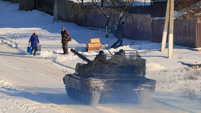 A Ukrainian tank patrols as locals receive humanitarian aid packages delivered by volunteers and by the Relief Service Ukraine of Order of Malta, in a village near Kupiansk in the Kharkiv area,