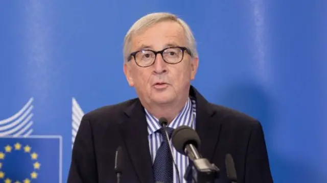 Jean-Claude Juncker close up as he stands in front of a lectern delivering speech in black suit, striped shirt and blue tie