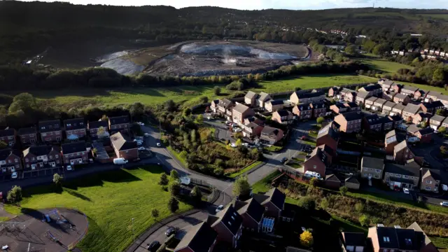 An aerial view of a landfill site on a field next to some houses.