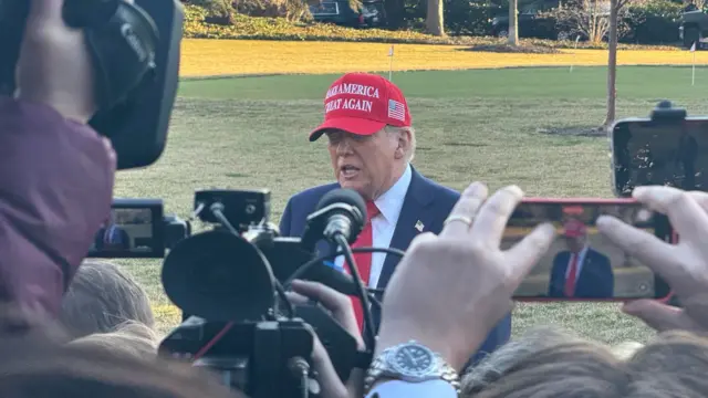 Trump in red MAGA cap in front of reporters