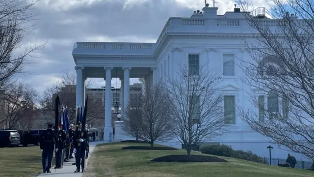 Two rows of men in uniform carrying flags outside the White House.
