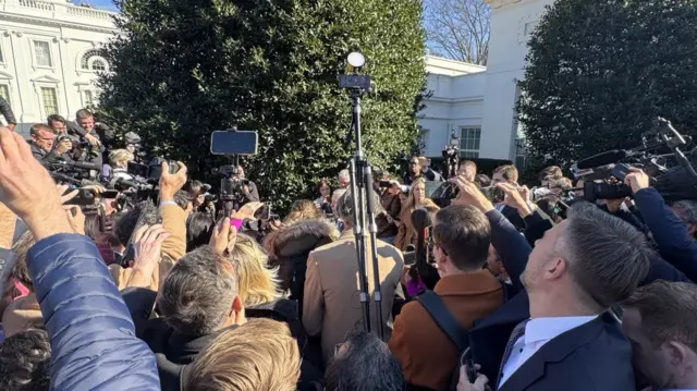 A huge group of reporters outside the White House, holding up cameras and phones.