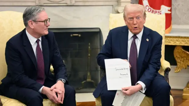 Trump (R) holds up a letter from King Charles III, given to him by Starmer (L). Both men are sitting on yellow chairs wearing dark blue suits