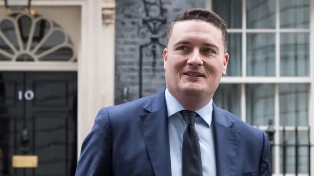 Wes Streeting facing the camera in a blue suit and black tie. Number 10 Downing Street front door in the background.