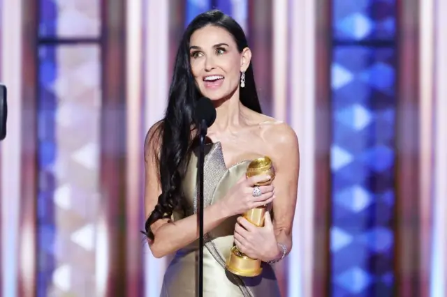 Demi Moore holding her golden globe at the ceremony in a golden dress