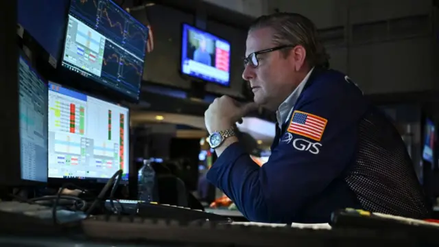 Traders work on the floor of the New York Stock Exchange (NYSE) in New York. A man is staring at several computer screens that show charts and figures.