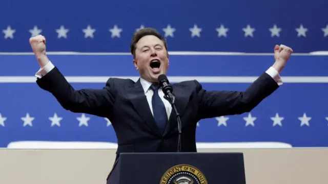 Elon Musk speaks at a Donald Trump rally on the day of the president's inauguration. He has his arms in the air and is speaking into a microphone.