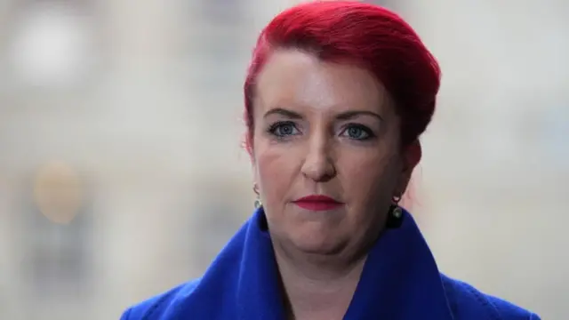 Louise Haigh, a woman with pink hair and wearing a blue coat, looks past the camera with a neutral expression