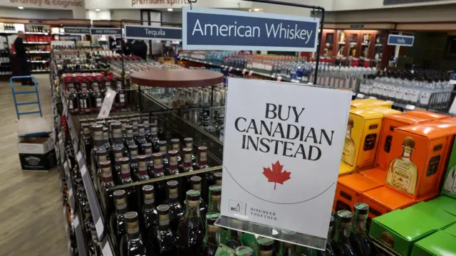 A sign reads 'Buy Canadian Instead' on an aisle for American Whisky