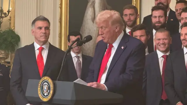 Donald Trump speaks at a podium surrounded by young men in suits, members of the 2024 NHL Florida Panthers Stanley Cup team