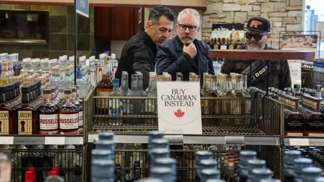 Men look at alcohol aisle, where there is a 'Buy Canadian Instead' sign