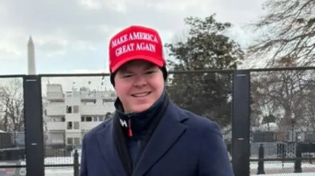 Charlie Kolean smiles at the camera, wearing a MAGA cap