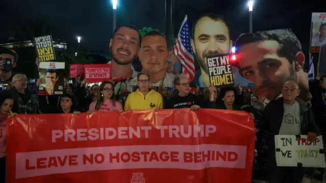 A number of people hold placards and images of hostages. A large banner at the fore of the group reads 'President Trump Leave no hostage behind'