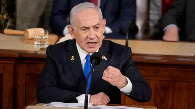 Netanyahu sits at a desk speaking into a microphone