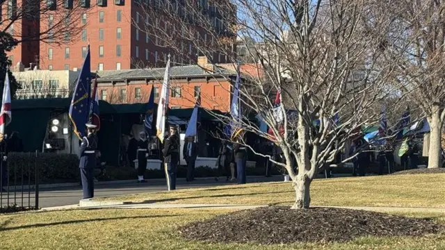 Military personnel holding flags line each side of the road