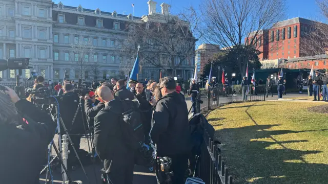 A crowd of reporters stand with camera equipment